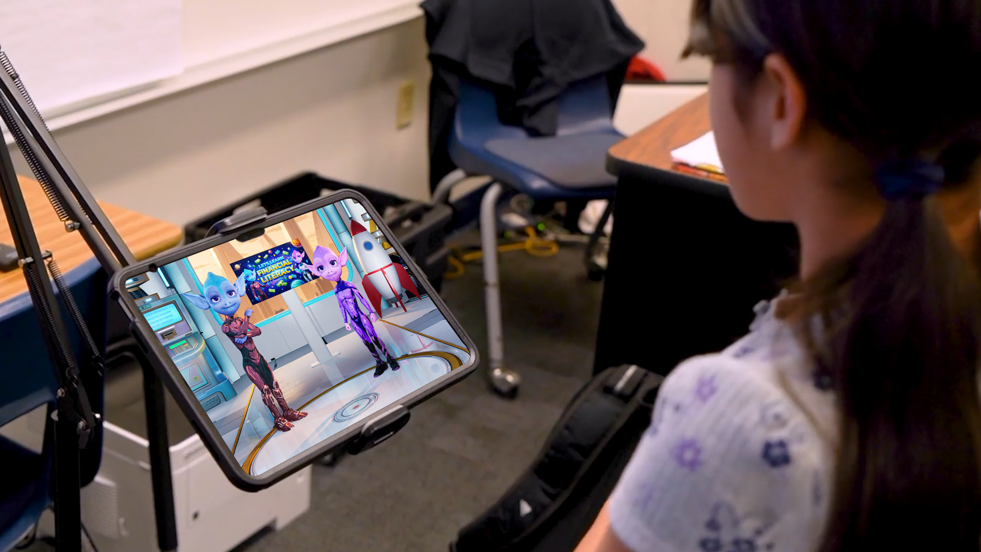 A student looking at a tablet showing two interactive characters in a financial literacy lesson